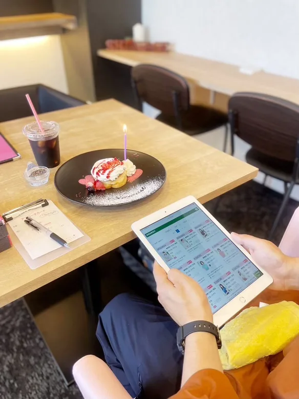 パンケーキとアイスコーヒーを前に、タブレットで会員一覧を見る手元とアプローチカード
