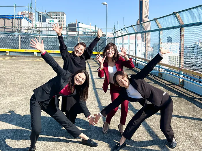 屋上で両手を広げてポーズをとる結婚相談所アイクルのスタッフ 4 名