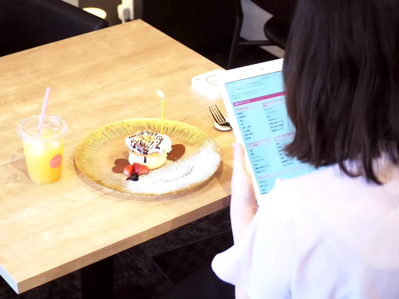 テーブルのパンケーキとジュースの横で、タブレットのプロフィールを読む女性