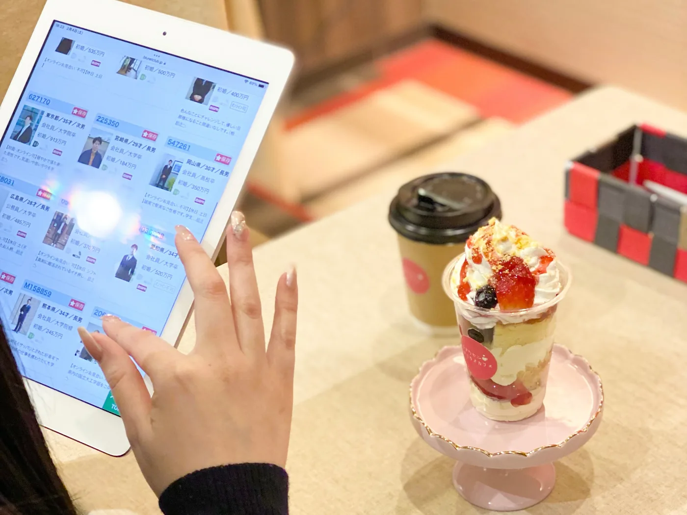 タブレットで会員のプロフィール一覧をスクロールする手元と、パフェとコーヒー
